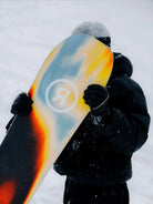 Snowboarder hält das Ride Vantum Snowboard 2026/27 im Schneefall, Belag mit Ride-Logo