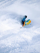 Snowboarder fährt mit dem Ride Vantum Snowboard 2026/27 eine Kurve im Tiefschnee